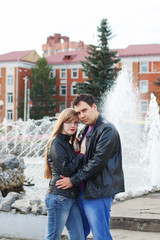 Man embraces woman in black leather jackets near fountain in aut