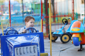 Happy cute little boy rides on car of carousel at summer day in