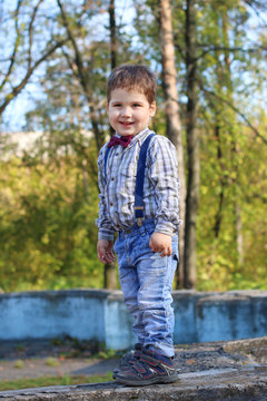 Plump little boy with bow tie and jeans stands in grimaces in su