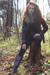Beautiful girl in boots and jacket poses on tree stump in sunny