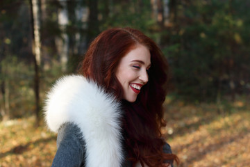 Pretty girl with make up and white fur laughs in forest at sunny