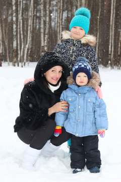 Happy mother with son, daughter in winter day during snowfall