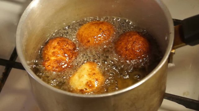 Round cheese donuts are fried in boiling oil in a frying pan