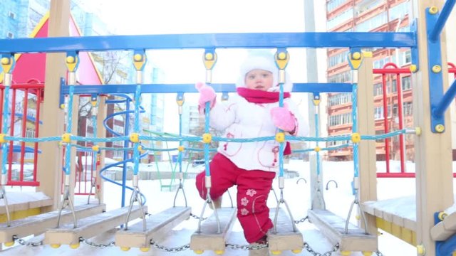 Happy little girl plays on playground at winter sunny day