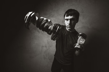 Fototapeta na wymiar Muscle man posing with dumbbells on wall backdrop. Black and white photo