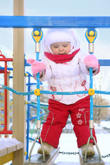 Happy little girl in white plays on playground at winter sunny d