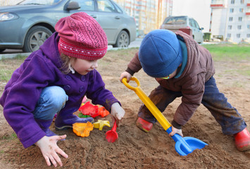 Happy little girl and boy play with plastic toys in sand outdoor