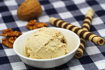 Scoop of creamy walnut ice cream with chocolate wafers on checkered cloth
