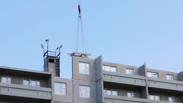 Part of grey apartment building of bearing-wall construction, hook of working crane with load