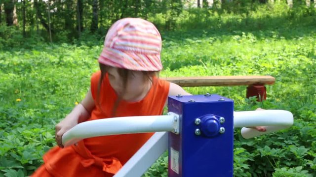 Little girl trains on outdoor exerciser in green summer park