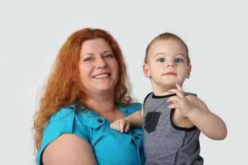 Happy redhead woman with her little son on hands ion gray background