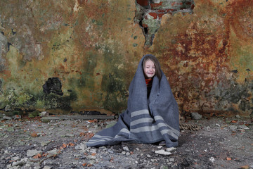 Little girl sits in basement wrapped in blanket and crying with tears on face - orphan, homelessness, poverty, despair concept