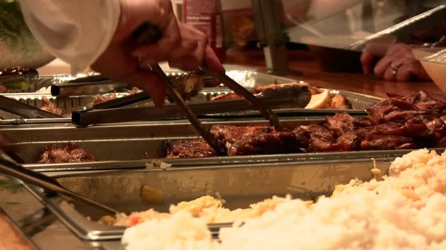 A 29 second close up clip of servers dishing up Hawaiian food from hot trays at a catering event. HD 1080i.