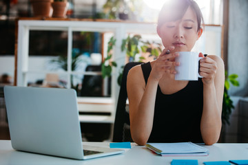 Relaxed young woman having coffee at her desk - Powered by Adobe