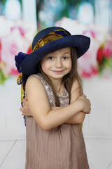 Cute little girl in too big hat smiles cringed with crossed arms