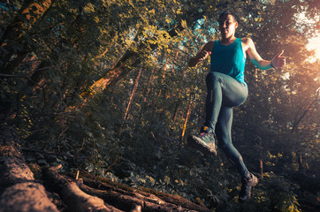 Trail running athlete jumping over wood barrier in the forest