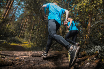 Two trial running athlete moving through the forest crossing wood barrier