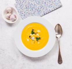 Pumpkin creamy soup in a white plate, top view