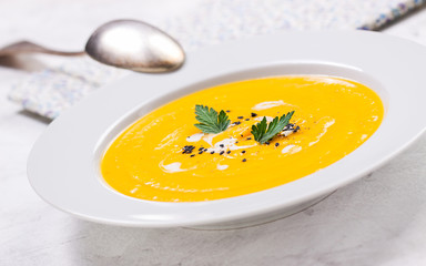 Pumpkin creamy soup in a white plate, closeup