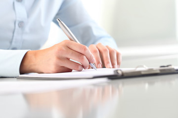 Woman's hands writing on clipboard with a pen; isolated on desk