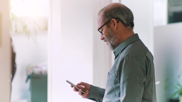 Businessman with smartphone in office reading message good news that makes him smile