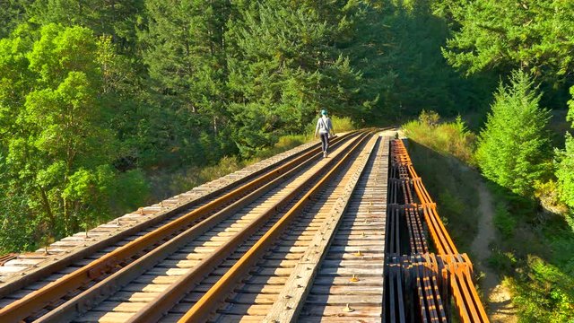 4K Woman Walks Across Old Wooden Rail Road Trestle, Tracks and Wood over River
