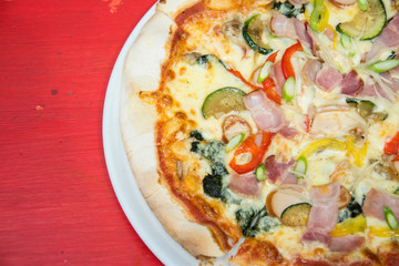 Hot pizza slice with melting cheese on red wooden table. 