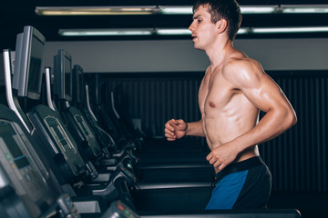 Fototapeta na wymiar Young man in sportswear running on treadmill at gym