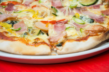 Hot pizza slice with melting cheese on red wooden table. 