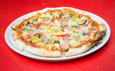 Hot pizza slice with melting cheese on red wooden table. 