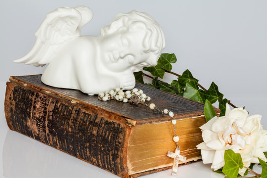 Alte Bibel mit Rosenkranz, Engel und weißer Rose