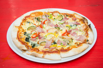 Hot pizza slice with melting cheese on red wooden table. 