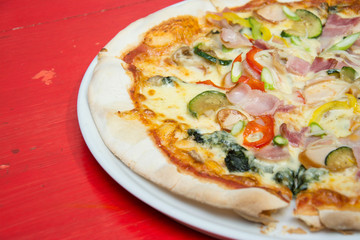 Hot pizza slice with melting cheese on red wooden table. 