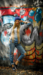 Fashionable girl with long blond hair in stylish clothes standing on a background of graffiti