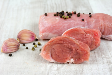 Raw pork meat with peppercorn and garlic on a wooden board.