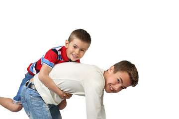 Older boy kneels and carries little brother on back isolated on square white background