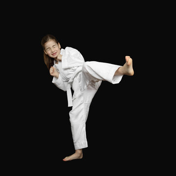 Overcoming of fear - little girl in sport white kimono with tight shut eyes beats foot on black background