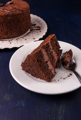 Chocolate cake with cream on a dark blue wooden table, with a spoon, copy space