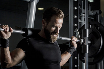 Hombre con grandes músculos levantando peso mientras entrena en el gimnasio. Ponerse en forma. - obrazy, fototapety, plakaty