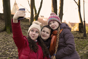 Three teenage girls stay together under one red umbrella outdoor on the natural autumn background