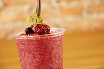 cold slushy fruity drink  on wooden tableRed fruit flavored frozen cocktail or smoothie beverage with straw and stirring stick