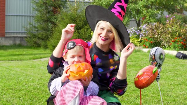 Mother and son in Halloween costumes having fun on Halloween party with jack latern pumpkin
