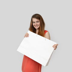 Young girl in red dress holds in hands shopping bag with blank space for text or logo on square gray background