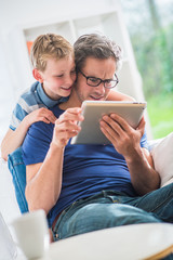  a father and his young son having fun by gaming on a tablet