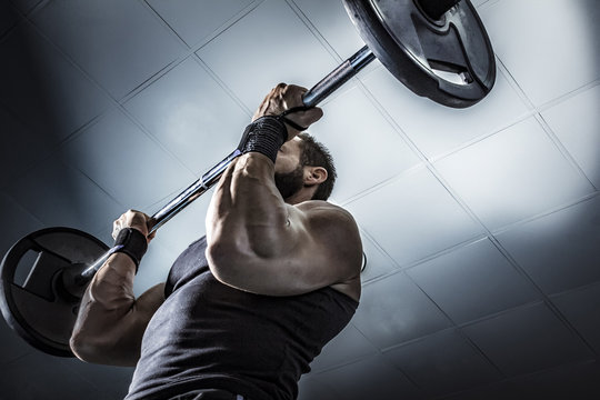 Hombre con grandes m&uacute;sculos levantando peso mientras entrena en el gimnasio. Ponerse en forma.