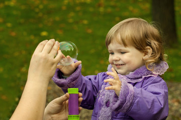 Little girl plays with soap bubbles outdoor on natural autumn background