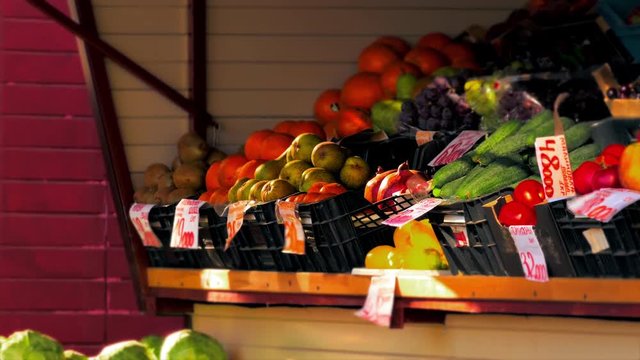 Lemons, tomatoes, oranges, pomegranates, kale, grapes with labels in Russian are on display in outdoor grocery stall.
