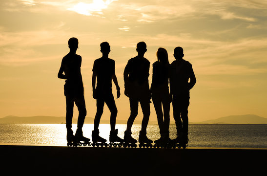 A group of teenage boys and a girl on roller skates at summer, silhouette. 