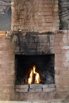 Old brick chimney - vintage looking rural fireplace with flame burning in furnace and sooty black front close up