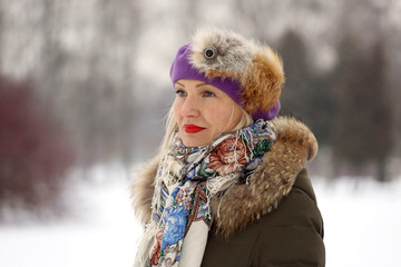 Fototapeta na wymiar Mature woman in purple beret and winter clothes on blur natural snowy background